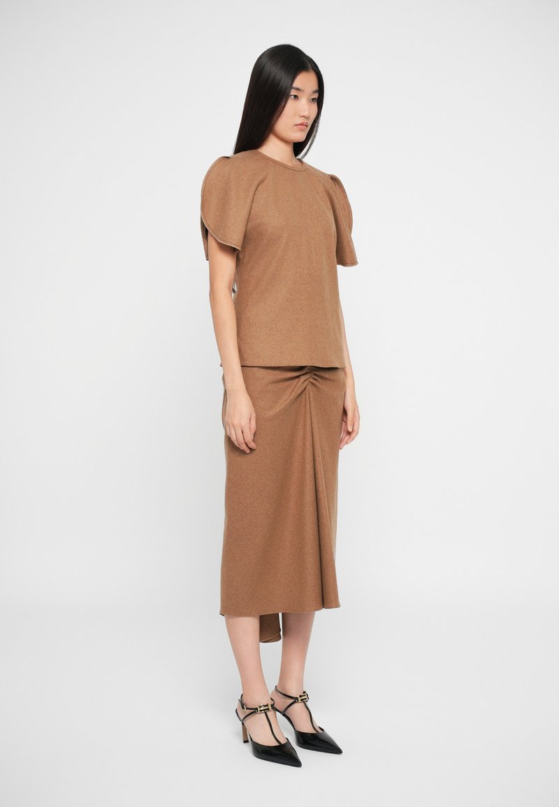 Top in maglia marrone con maniche a sbuffo abbinato a una gonna coordinata con dettaglio torcido, completato da eleganti tacchi a punta neri.