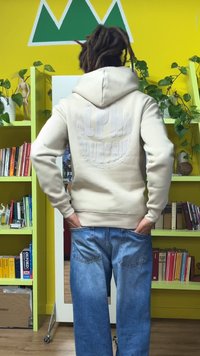 Sweatshirt bege com um logótipo texturizado "ALPHA INDUSTRIES" nas costas, combinado com jeans de ganga azul clara com bolsos traseiros visíveis.