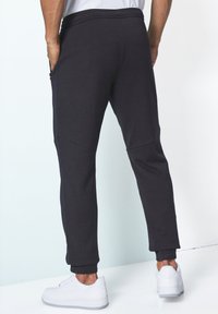 Schwarze Jogginghose mit schmal zulaufenden Beinen, elastischen Bündchen und Seitentaschen, aus weichem Material gefertigt, mit nahtlosem Design auf der Rückseite.