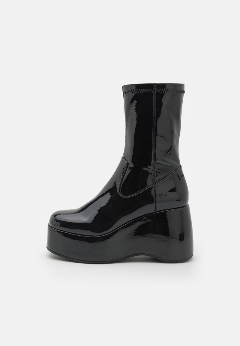 Bottine noire brillante à plateforme avec semelle compensée haute, tige mi-mollet, bout arrondi lisse et détails de coutures.