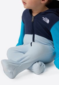 Kombinezon z polaru w kolorze granatowym i jasnoniebieskim, z zamkiem z przodu i kapturem. Miękka faktura z kontrastowymi górną i dolną częścią.