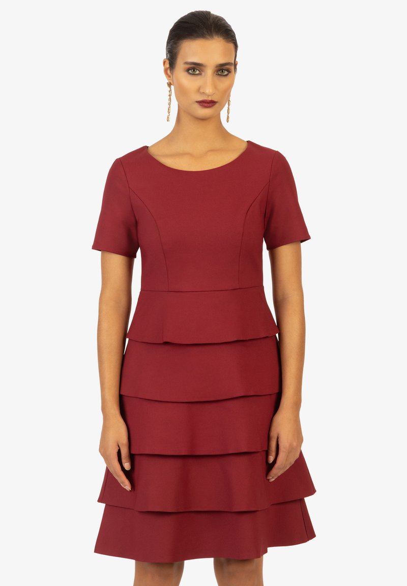 Robe ajustée bordeaux avec manches courtes, présentant un design à volants et une texture lisse. Encolure ronde et ourlet superposé.