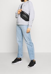 Sudadera gris claro con puños acanalados, jeans de talle alto azules y zapatillas negras. Riñonera negra llevada alrededor de la cintura con un bolsillo con cremallera.