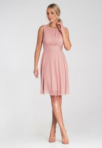 Jasnoróżowa sukienka bez rękawów z marszczoną górą i zwiewnym dołem. Posiada talię i przezroczysty overlay, zestawiona z cielistymi sandałami na obcasie.