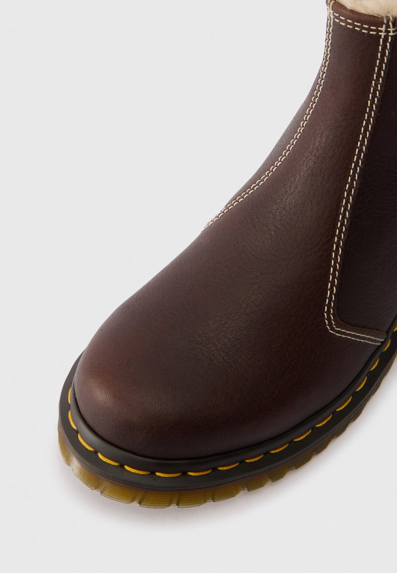 Primo piano di un stivale di pelle marrone con cuciture gialle e suola di gomma traslucida su sfondo bianco.