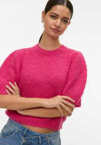 Pull court rose avec une texture douce et duveteuse, encolure ronde et manches courtes bouffantes, associé à un jean en denim bleu.