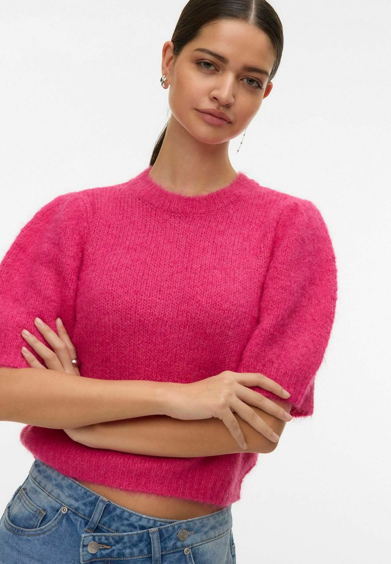 Pull court rose avec une texture douce et duveteuse, encolure ronde et manches courtes bouffantes, associé à un jean en denim bleu.
