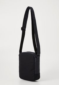 Borsa a spalla in tessuto nero con una tracolla regolabile, caratterizzata da cuciture blu. Forma rettangolare con chiusura a zip e superficie texturizzata.