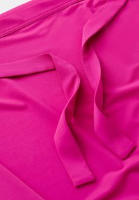 Tissu rose vif avec deux longues lanières plates disposées sur une surface lisse, montrant la texture et les détails des coutures.