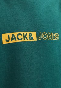 T-shirt verde con la scritta "JACK & JONES" stampata in giallo e verde scuro. Tessuto liscio con un collo in stile standard.