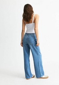 Jeans de pierna ancha de color azul claro con una cinturilla elástica fruncida, que cuentan con dos bolsillos traseros y una textura de denim suave. Top sin mangas blanco sencillo.