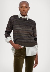 Dark knit sweater with multicolored horizontal stripes, paired with a white and blue striped shirt. Olive green corduroy pants complete the look.
