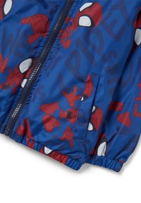 Blauwe ritsjack gemaakt van glanzend materiaal, met een Spider-Man patroon en rode en witte accenten. Inclusief een elastische tailleband en een zak.