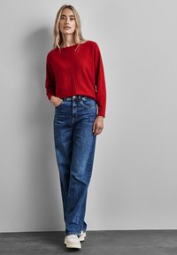 Röd långärmad tröja med rundad halsringning, parat med blå högmidjade raka jeans. Vita sneakers fulländar outfiten.