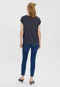 Tmavě šedý krátký rukáv s volným střihem, v kombinaci s modrými úzkými džíny a černými muly na podpatku, pohled zezadu.