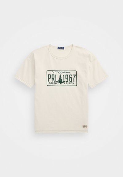 Crème katoenen T-shirt met korte mouwen. Heeft een groene grafische print met de teksten "OUTDOORSMAN," "PRL 1967," en een dennenboomontwerp.