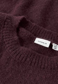 Burgundy stickad tröja med ribbad halslinning och mjuk textur. Har en etikett med "name it" och storleksinformation fäst.