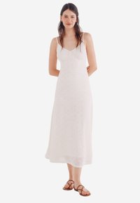 Robe maxi blanche avec un corsage ajusté et un motif texturé. Bretelles réglables et silhouette fluide. Sandales marron incluses.