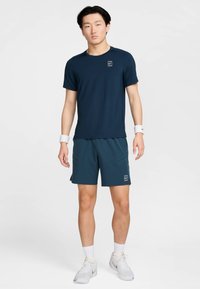 Mörkblå sport-t-shirt och matchande shorts av lättviktstyg, med en liten logotyp och fickor framtill, bärs med vita sneakers.
