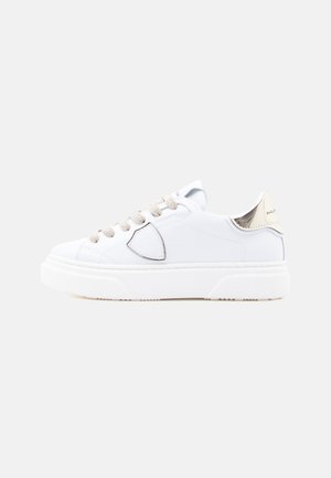 Sneaker in pelle bianca con dettagli argento, lacci strutturati e suola spessa bianca. Presenta una punta arrotondata e un logo sul tallone.