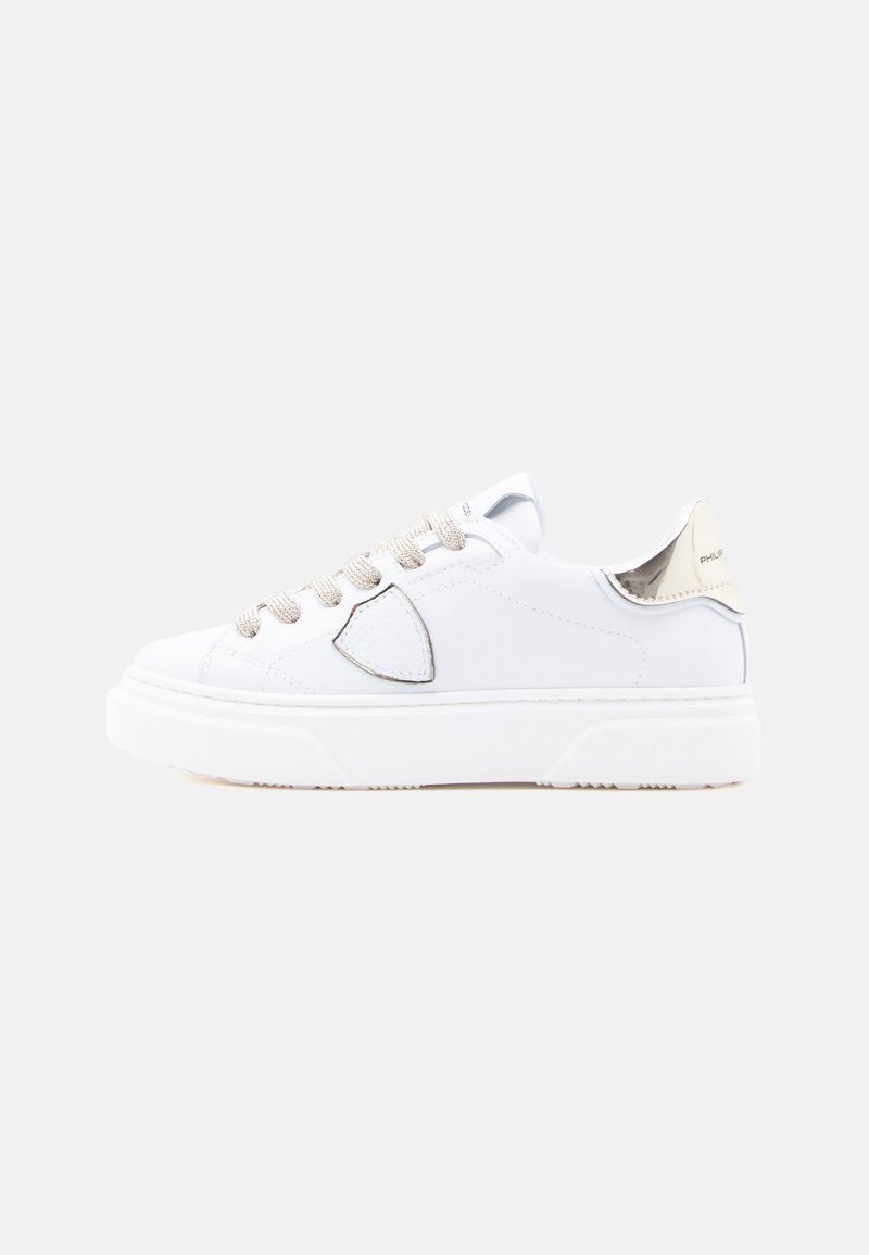 Λευκό δερμάτινο αθλητικό παπούτσι με ασημί λεπτομέρειες, υφασμένα κορδόνια και χοντρή λευκή σόλα. Διαθέτει στρογγυλερή μύτη και λογότυπο στην φτέρνα.