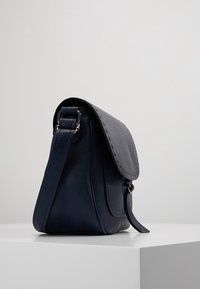 Granatowa skórzana torebka na ramię z klapką na górze, regulowanym paskiem i widocznymi szwami. Boczną kieszonką dla zwiększenia funkcjonalności.