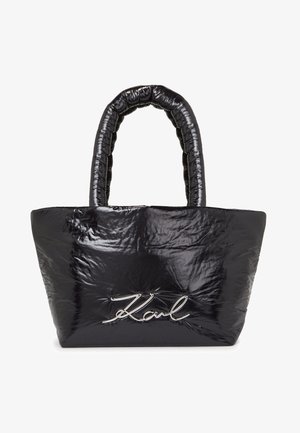 Czarna pufasta torba tote z textured, błyszczącym materiałem i wyróżniającym się logo w srebrnym stylu na przedniej stronie. Posiada wyściełany uchwyt.