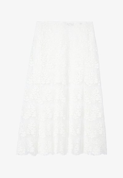 Jupe en dentelle blanche avec un design superposé, présentant des motifs floraux et un ourlet en vagues. Fabriquée en tissu léger et texturé.