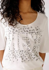 Witte t-shirt met korte mouwen, voorzien van een zilveren luipaardprintpatroon en de tekst "HEY" versierd met kleine strass-steentjes. Glad textuur van de stof.