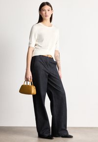 Svetlo kremast pulover z kratkimi rokavi iz pletenine, kombiniran s temnimi širokimi kavbojkami in majhno rumeno torbico. Črne koničaste čevlje dopolnjujejo videz.