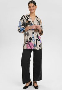 Chemise à boutons multicolore avec des motifs abstraits en noir, bleu et rose ; tissu léger ; associée à un pantalon large noir et des chaussures.