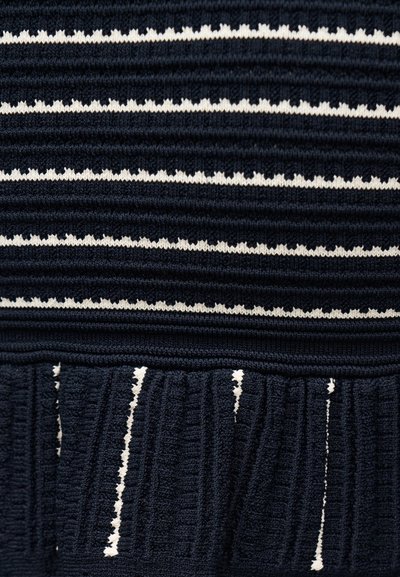 Σκούρο μπλε πλεκτό ύφασμα με οριζόντιες λευκές ζιγκ ζαγκ ρίγες και κάθετη ραβδωτή υφή στο κάτω τμήμα.