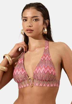 Young woman wearing pink and brown zigzag halter bikini top with gold buckle, large gold hoop earrings, and gold bracelets.