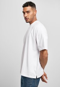 T-shirt bianco in cotone con vestibilità rilassata, maniche corte e fessure laterali. Abbinato a jeans di denim blu. Design minimalista, senza fantasia.