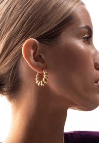 Złoty spirale kolczyk w kształcie obręczy z teksturowaną powierzchnią, z zaokrąglonymi krawędziami i polerowanym wykończeniem. Przezroczyste tło podkreśla wzór.