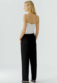 Witte camisole met dunne bandjes, gecombineerd met hoge zwarte broeken; gladde stof met een getailleerde pasvorm en zijzakken.