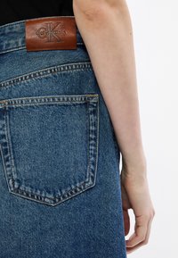 Jeansrock mit blauer Waschung, Gesäßtasche und einem braunen Lederlabel von Calvin Klein am Bund. Glatte Textur und klassisches Design.