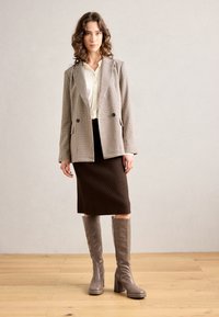 Dwurzędowa marynarka w wzór houndstooth w odcieniach beżu i czerni; kremowa bluzka; brąskowa spódnica z prążkami; szare kozaki do kolan na obcasie.