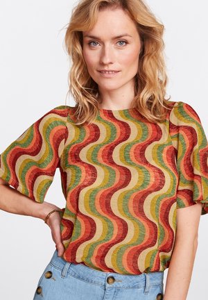 Blusa de manga corta con un patrón ondulado en rojo, verde y amarillo sobre una tela texturizada. Cuello redondo y diseño de corte relajado.