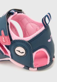 Blå och rosa sandal med rundad form, mjukt tyg, utskurna sidor och en liten logotypdetalj på sidan. Lättviktig design för komfort.