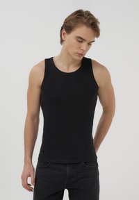 Top a maniche corte nero a coste con scollatura rotonda; design aderente; abbinato a jeans scuri; texture liscia e stile minimalista.