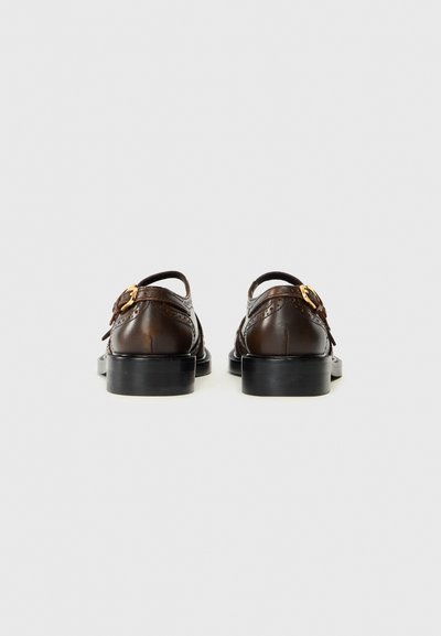 Bruine leren schoenen met decoratieve brogue-details, een gespstrap en een lage zwarte hak, bekeken vanuit de achterkant. Glad oppervlak.
