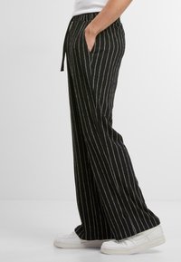 Pantaloni cu dungi negre, iară largi, dintr-un material moale. Disponibil cu un tiv elastic și șnur, plus buzunare laterale, completate cu adidași albi.