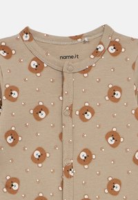 Body de bebé em tom bege com padrão de rostos de ursos e pegadas. Apresenta decote redondo, fecho frontal com botões e tecido macio e texturizado.