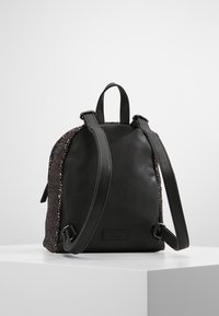 Sac à dos noir avec un devant en cuir lisse et un dos en tissu texturé et scintillant. Équipé de bretelles doubles réglables et d'une poignée supérieure.