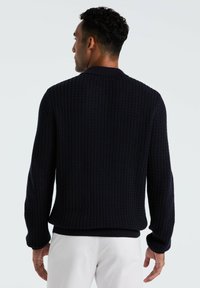 Marineblauer Strickpullover mit einem strukturierten Muster, gerippten Bündchen und Saum. Verfügt über einen klassischen Kragen und wird mit hellen Hosen getragen.