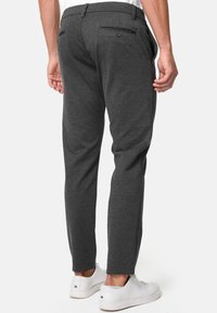 Pantalones gris oscuro con una tela suave, corte entallado, dos bolsillos traseros con botones, y combinados con zapatillas blancas.