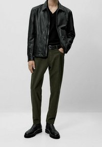 Musta nahkatakki mustan v-kaula-aukkoneuleen päällä, yhdistetty oliivinvihreisiin housuihin ja mustiin Chelsea-saappaisiin.