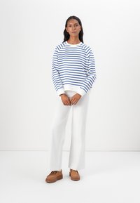 Maglione a righe blu e bianche con scollatura rotonda, abbinato a pantaloni bianchi a gamba larga e scarpe con piattaforma marroni.