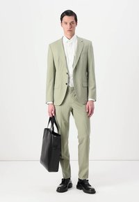 Traje verde claro de diseño ajustado, combinado con una camisa blanca. Un bolso y zapatos de cuero negro completan el look. Textura de tejido suave.
